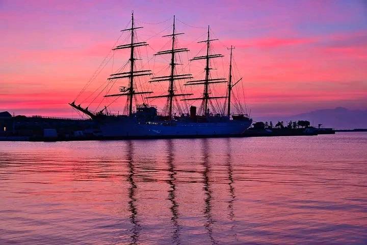 夕陽に染まる港に停泊する帆船のシルエット